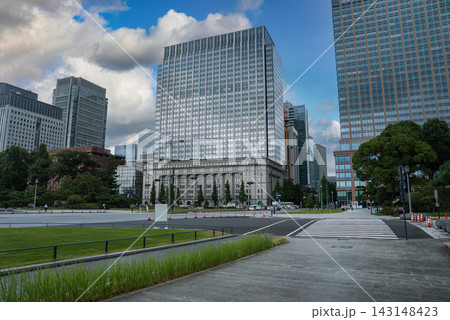 A plaza and crosswalk lead to glass towers in Tokyo Marunouchi near the Imperial Palace and Tokyo Station, with manicured lawns, stone facade, and light pedestrian flow. A plaza and crosswalk lead to glass towers in Tokyo Marunouchi near the Imperial Palace and Tokyo Station, with manicured lawns, stone facade, and light pedestrian flow. 143148423