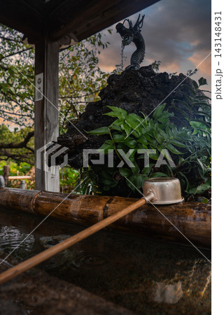 A temizuya at a Tokyo shrine shows a coiled dragon spout pouring into a bamboo trough, a wooden ladle on the rim, and a small pavilion with garden leaves in view. A temizuya at a Tokyo shrine shows a coiled dragon spout pouring into a bamboo trough, a wooden ladle on the rim, and a small pavilion with garden leaves in view. 143148431