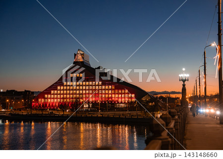 Riga, Latvia, dusk view of the National Library of Latvia glowing red, windows form a grid, reflections on the Daugava River, streetlights and traffic move along the embankment Riga, Latvia, dusk view of the National Library of Latvia glowing red, windows form a grid, reflections on the Daugava River, streetlights and traffic move along the embankment 143148660