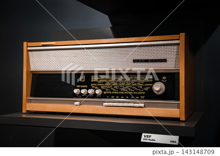 Close up of a wooden VEF Radio 1965 on a dark museum shelf, with silver mesh grille, Cyrillic station markers, white knobs, and tight studio style composition. Close up of a wooden VEF Radio 1965 on a dark museum shelf, with silver mesh grille, Cyrillic station markers, white knobs, and tight studio style composition. 143148709