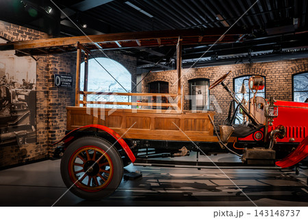 An early 20th century red fire truck with wood panels and ladder frame stands in a museum setting with brick walls, arched windows, brass fittings, spoked wheels, and gallery lighting. 143148737