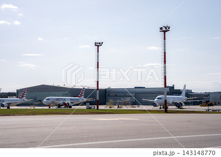 Daytime view of narrow body jets parked before FL Technics hangars at Vilnius Airport, Lithuania. HESTON and WingsSafe titles appear near two tall red and white towers. 143148770