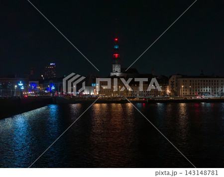 Evening view across the Daugava shows Riga Old Town and Riga Castle tower lit red and blue. Streetlights reflect on water as traffic lines the embankment during events. Evening view across the Daugava shows Riga Old Town and Riga Castle tower lit red and blue. Streetlights reflect on water as traffic lines the embankment during events. 143148781