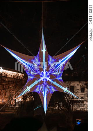 A star shaped installation glows with blue and violet patterns in Riga, Latvia, during Staro Riga 2025. Night lighting, high contrast, historic facades faintly visible. A star shaped installation glows with blue and violet patterns in Riga, Latvia, during Staro Riga 2025. Night lighting, high contrast, historic facades faintly visible. 143148815