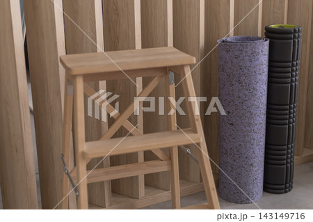 Wooden step ladder next to rolled yoga mat and foam roller 143149716