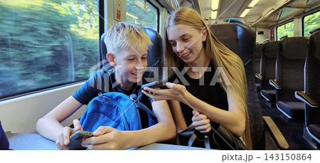 Smiling teenage girl and young boy using smartphones while traveling on a train 143150864