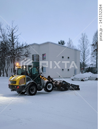 A snowplow is clearing snow from the street in front of the houses. A snowplow is clearing snow from the street in front of the houses. 143152264