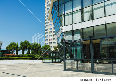 Modern building with large glass windows and paved outdoor area in a sunny setting Modern building with large glass windows and paved outdoor area in a sunny setting 143158561