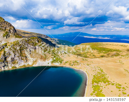 Scenic view of a mountain lake surrounded by rocky terrain and grassy slopes under a cloudy sky in a remote area Scenic view of a mountain lake surrounded by rocky terrain and grassy slopes under a cloudy sky in a remote area 143158597
