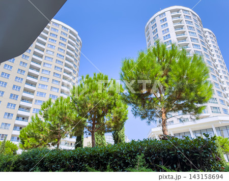 Tall buildings stand beside green trees in a bright blue sky during the day at a modern residential area Tall buildings stand beside green trees in a bright blue sky during the day at a modern residential area 143158694