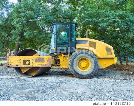 Construction equipment is on a job site with trees in the background and gravel under the machine on a clear day Construction equipment is on a job site with trees in the background and gravel under the machine on a clear day 143158730