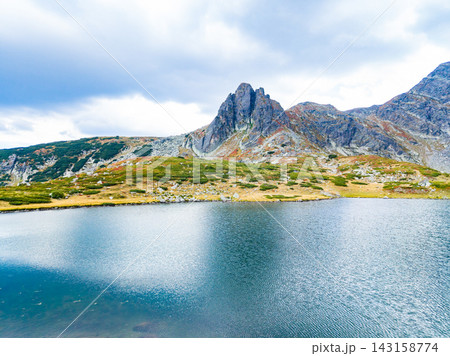 Mountains reflect in the water of a lake under a cloudy sky in a natural landscape setting 143158774