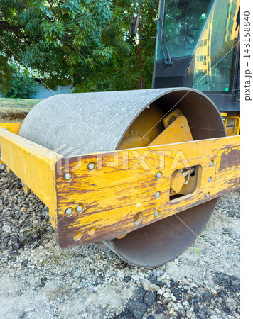 Construction equipment is parked at a work site with a yellow roller on a gravel surface in a city area during the day Construction equipment is parked at a work site with a yellow roller on a gravel surface in a city area during the day 143158840