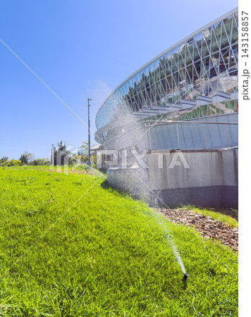 Watering the grass near a modern building on a sunny day in a landscaped area with clear blue skies Watering the grass near a modern building on a sunny day in a landscaped area with clear blue skies 143158857