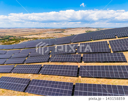 Solar panels cover a large area on a sunny day in an open field with blue sky and clouds 143158859