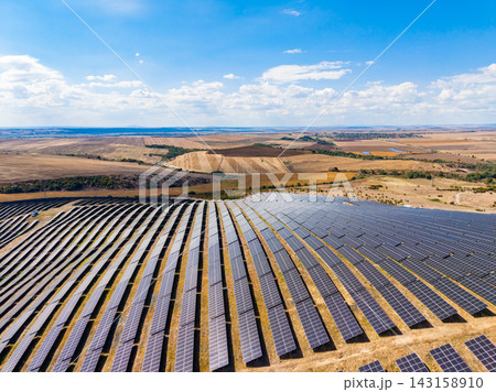 Solar panels cover a large area in a renewable energy farm during the day in a rural landscape with fields and hills 143158910