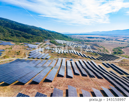 Solar panels cover an expansive area in a sunny landscape with mountains in the background during the daytime Solar panels cover an expansive area in a sunny landscape with mountains in the background during the daytime 143158997