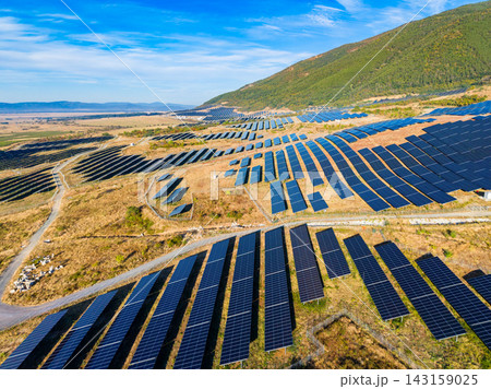 Large solar panel farm on a hillside in a rural area with blue sky and mountains in the background in the daytime 143159025