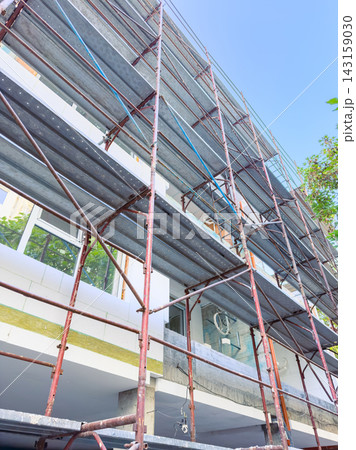 Construction work takes place on a building with scaffolding in daylight at a construction site 143159030