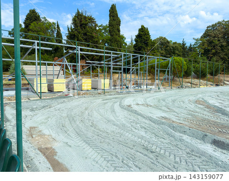 Construction of a new building structure near a park with various trees under a clear blue sky in the midday 143159077