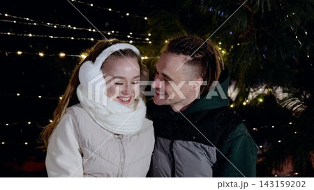 Young couple sharing tender gaze under twinkling christmas lights, snowflakes falling softly around embracing partners, capturing intimate winter romance Young couple sharing tender gaze under twinkling christmas lights, snowflakes falling softly around embracing partners, capturing intimate winter romance 143159202