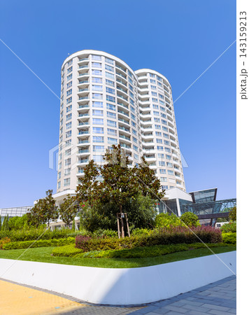 Modern building stands tall under clear blue sky in the daytime with landscaped gardens in front 143159213