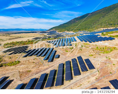 Solar panels cover a large field in a rural area surrounded by hills under a clear blue sky 143159294