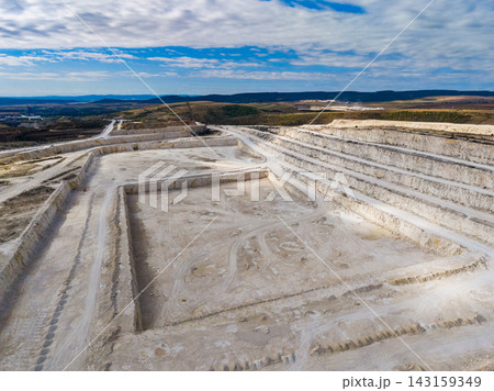 Quarry site with layered earth and machinery on a clear day near a mountain landscape 143159349