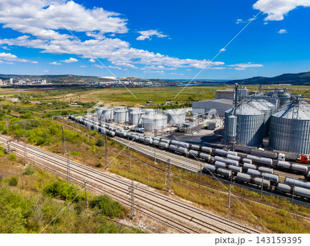 Large industrial site with storage silos and train tracks near a water body on a clear day 143159395