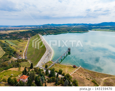 Distant view of a dam and reservoir surrounded by hills and fields under a cloudy sky Distant view of a dam and reservoir surrounded by hills and fields under a cloudy sky 143159470