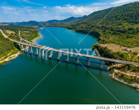 Bridge spans a large body of water surrounded by hills and green trees on a clear day Bridge spans a large body of water surrounded by hills and green trees on a clear day 143159476