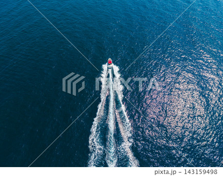 Small boat moving across water with wake and ripples in bright blue sea under clear sky Small boat moving across water with wake and ripples in bright blue sea under clear sky 143159498