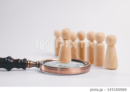 Wooden figure standing on a magnifying glass before a group, representing recruitment, candidate assessment, talent selection, hiring, leadership, human resources, evaluation, and career opportunity. 143160066