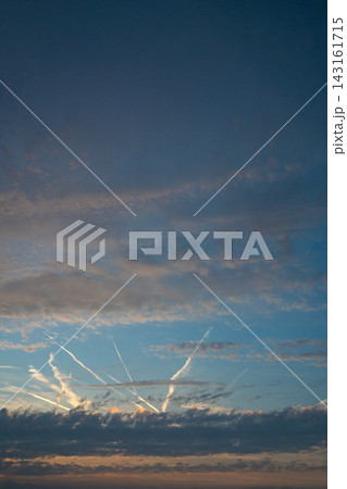 Dramatic sunset sky with layered dark clouds and illuminated airplane contrails crossing a blue and orange horizon. 143161715