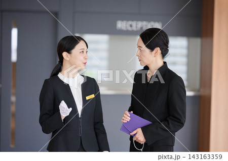 斎場の受付で参列者に案内をする女性スタッフ 143163359