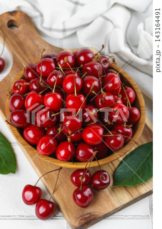 Fresh ripe sweet cherry in wooden bowl on rustic cutting board with green leaves on white background 143164491