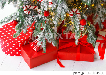 Red wrapped gift boxes, presents under festive Christmas tree with lights and holiday decorations Red wrapped gift boxes, presents under festive Christmas tree with lights and holiday decorations 143164514