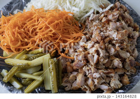 Ingredients for homemade shawarma or kebab on a plate: chopped chicken meat, shredded white cabbage, fresh grated carrots, and sliced pickles ready for cooking wrap. 143164828