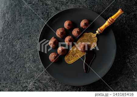 Chocolate truffles and vintage brass cake server on a black plate. 143165416