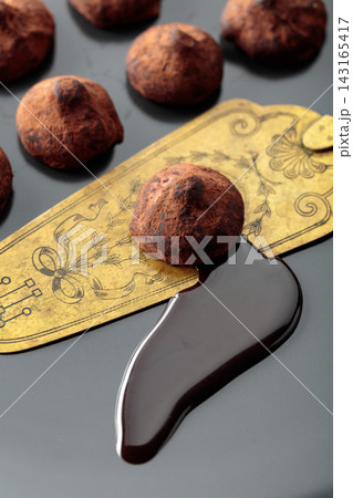 Chocolate truffles, chocolate sauce, and vintage brass cake server on a black plate. 143165417