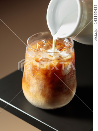 Cream is poured into a glass of iced coffee. Cream is poured into a glass of iced coffee. 143165435