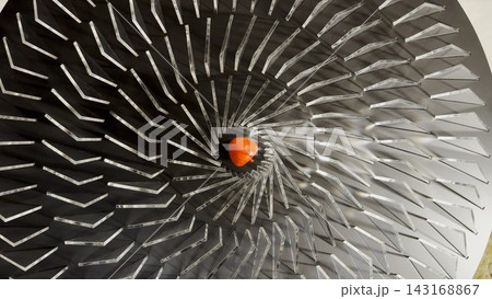 Top view on spiral geometric installation with metallic radial elements surrounding a red apple-shaped object in the center. Strong symmetry, depth and optical movement create a striking visual focus Top view on spiral geometric installation with metallic radial elements surrounding a red apple-shaped object in the center. Strong symmetry, depth and optical movement create a striking visual focus 143168867