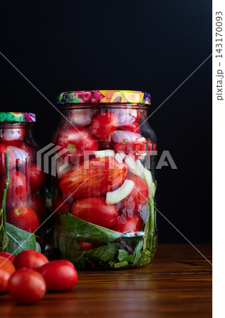 Preserved red tomatoes with herbs in jars on black background Preserved red tomatoes with herbs in jars on black background 143170093