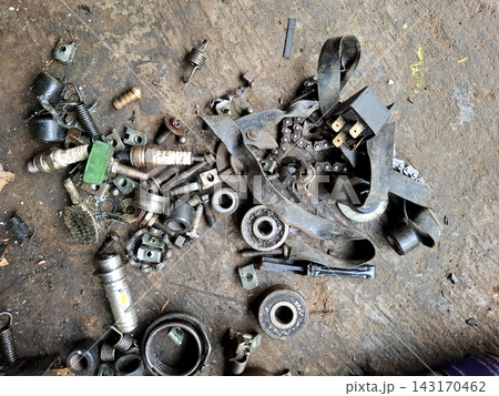 Scattered motorcycle mechanical parts including metal bolts small springs electrical relay and drive chain pieces lying on dirty workshop floor for engine repair. Scattered motorcycle mechanical parts including metal bolts small springs electrical relay and drive chain pieces lying on dirty workshop floor for engine repair. 143170462