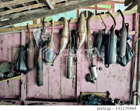 Collection of various metal motorcycle exhaust pipes hanging on pink wooden wall in rustic workshop for vehicle repair maintenance and custom bike customization. 143170464