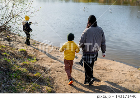 Parent and child walking hand in hand along sandy lakeshore with gulls in flight under warm autumn afternoon light, calm water reflections, and quiet outdoor nature Parent and child walking hand in hand along sandy lakeshore with gulls in flight under warm autumn afternoon light, calm water reflections, and quiet outdoor nature 143171440