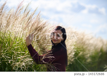 Smiling woman standing among tall ornamental grass on sunny autumn day Smiling woman standing among tall ornamental grass on sunny autumn day 143172686