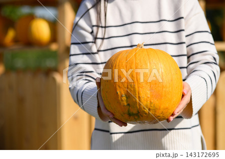 Woman holding large orange pumpkin with both hands at autumn pumpkin patch Woman holding large orange pumpkin with both hands at autumn pumpkin patch 143172695
