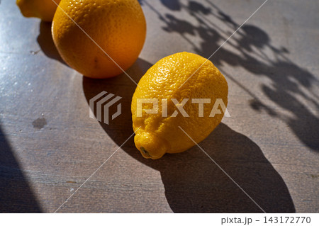 Fresh lemons on rustic wooden table with sharp sunlight shadows, close-up food ingredient for summer cooking, lemon zest and juice for lemonade, healthy citrus breakfast concept 143172770