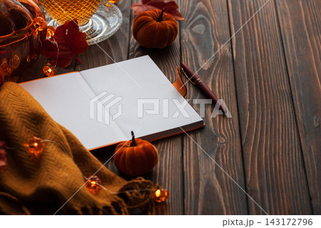 Cozy autumn scene with open notebook, warm drink, pumpkins, and fairy lights on wooden table 143172796